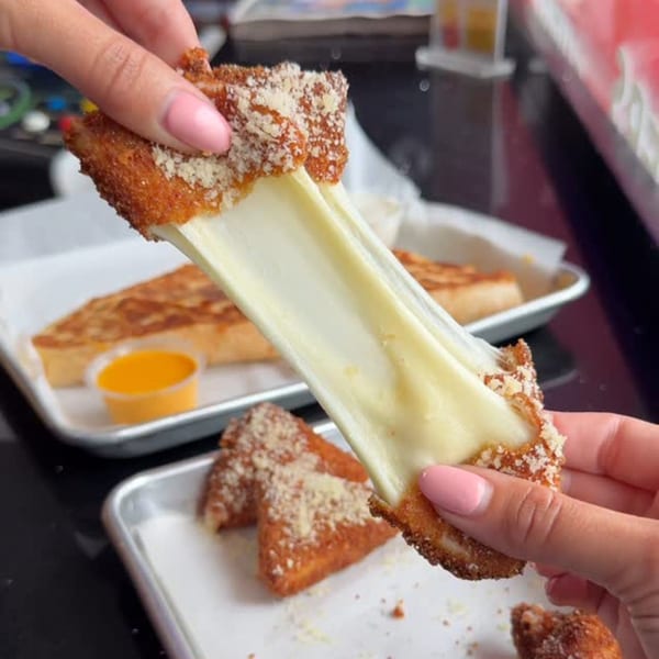 Hands pulling apart a crispy, breaded grilled cheese sandwich, revealing long, stretchy melted cheese.