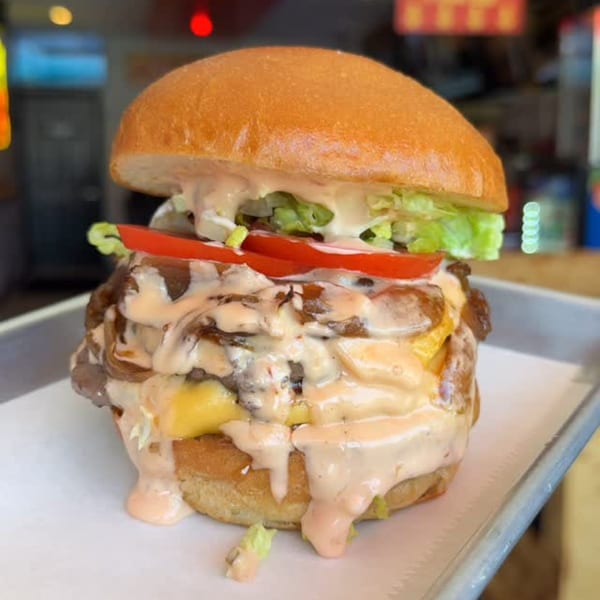 A BRENDOS sandwich with melted cheese, lettuce, tomatoes, and sauce dripping down the sides.