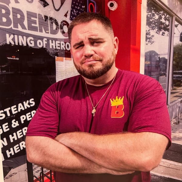 Man in a Brendo's King of Hero t-shirt with crossed arms stands outside the restaurant.