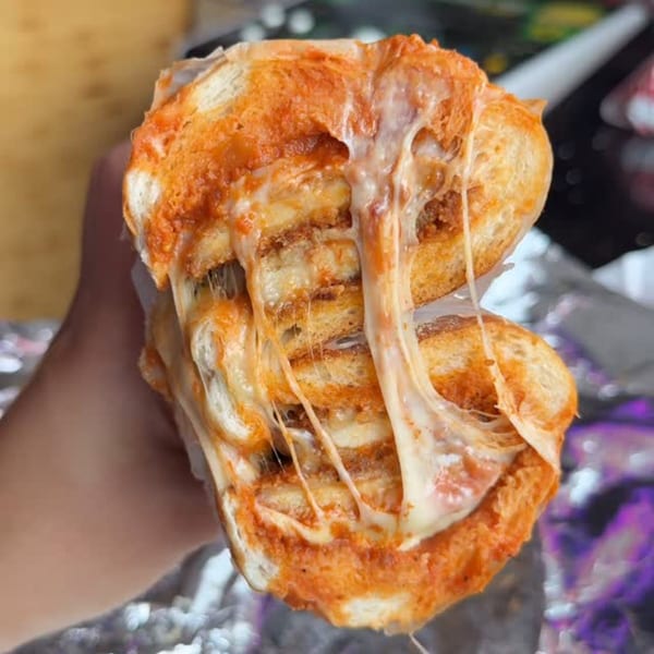 A hand holds a BRENDOS sandwich, overflowing with melted cheese and red sauce.
