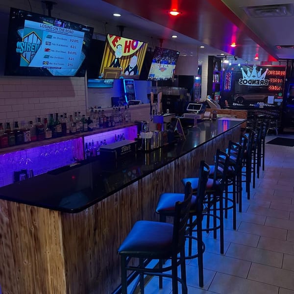 Brendos bar with purple lighting, bar stools, liquor bottles, and TVs showing sports and cartoons.