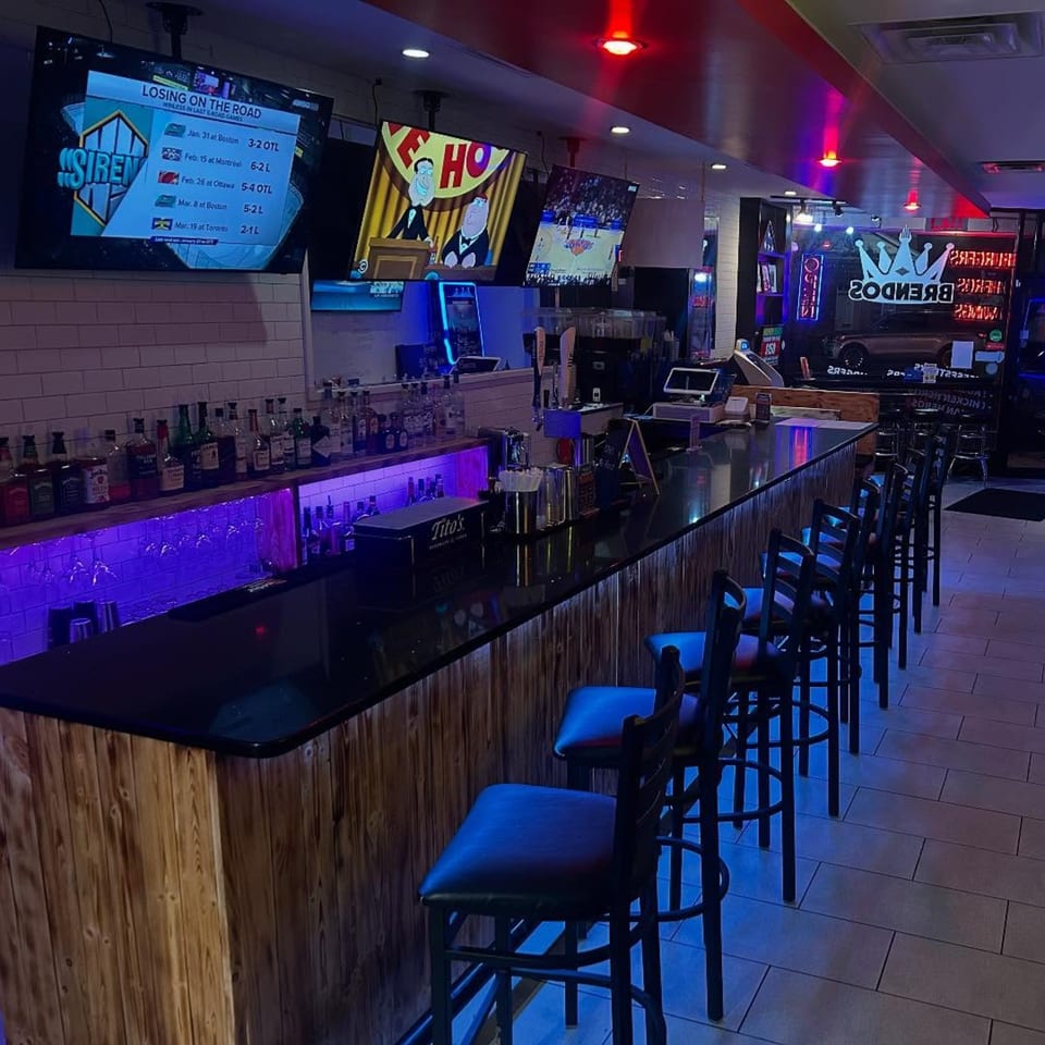 Brendos bar with purple lighting, bar stools, liquor bottles, and TVs showing sports and cartoons.
