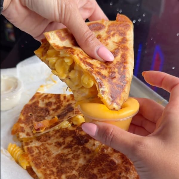 Hands dipping a BRENDOS mac and cheese quesadilla into a small cup of cheese sauce.