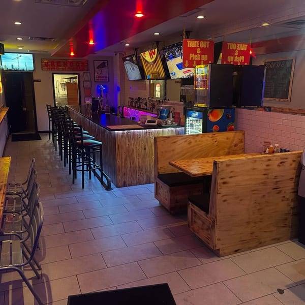 Interior of BRENDOS restaurant with a long bar, stools, wooden booths, and TVs showing sports.